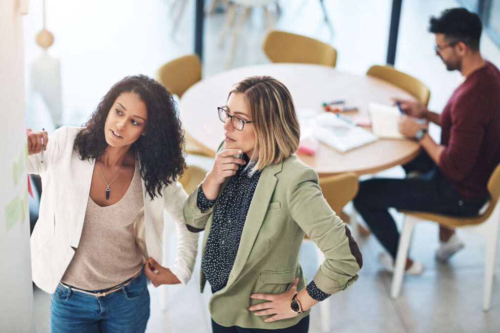 two women stand and look at an office whiteboard during a brand strategy and planning session