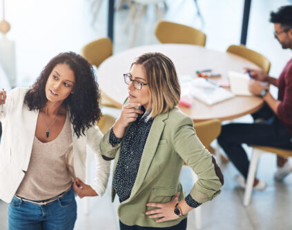 two women stand and look at an office whiteboard during a brand strategy and planning session
